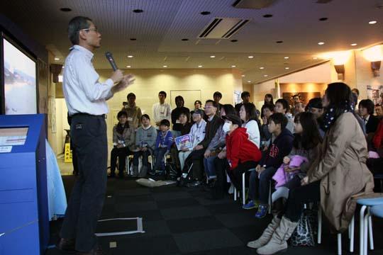 JAXA相模原キャンパスで行われた「はやぶさ２」パブリックビューイングで司会者の言葉を聞く参加者の写真